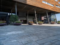 a concrete courtyard with pots of plants and a building that has a wooden roof on it