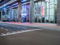 an outside view of a modern building at night with red and blue lights on the outside