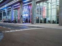 an outside view of a modern building at night with red and blue lights on the outside