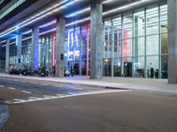 an outside view of a modern building at night with red and blue lights on the outside