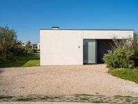 a building that is standing in gravel near trees and shrubs that have grass on it