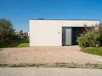 a building that is standing in gravel near trees and shrubs that have grass on it