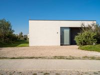 a building that is standing in gravel near trees and shrubs that have grass on it