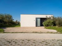 a building that is standing in gravel near trees and shrubs that have grass on it