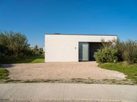 a building that is standing in gravel near trees and shrubs that have grass on it