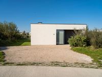 a building that is standing in gravel near trees and shrubs that have grass on it