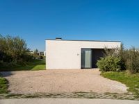 a building that is standing in gravel near trees and shrubs that have grass on it