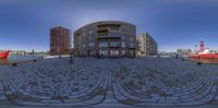 a fish eye lens shows a building in the middle of a small riverfront with boats