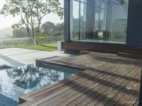 a wooden deck overlooks a small pool in the sun near a house with large sliding glass doors