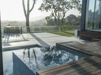 a wooden deck overlooks a small pool in the sun near a house with large sliding glass doors