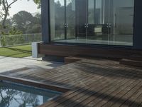 a wooden deck overlooks a small pool in the sun near a house with large sliding glass doors