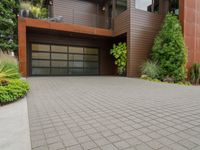 a home with wood panels and gray windows and a brick driveway and a stone paved walkway