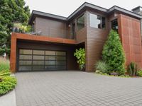 a home with wood panels and gray windows and a brick driveway and a stone paved walkway