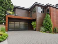 a home with wood panels and gray windows and a brick driveway and a stone paved walkway