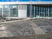 a paved area outside of an office building with a clock on it and a stairway going down to the side