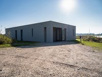 a building with a door and no windows sitting on the side of a dirt field