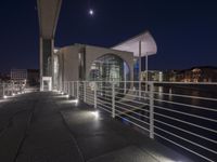 a building and its walkway near a river at night and illuminated up with lights in the dark