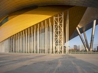 a yellow metal structure next to a large brick building and white columns and walls around it