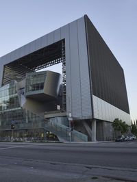 a modern architecture designed in the middle of the street with cars parked near it in the sunset