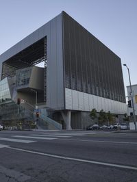 a modern architecture designed in the middle of the street with cars parked near it in the sunset