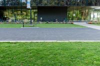 a large glass building next to a green park and grass area with benches on the walkway