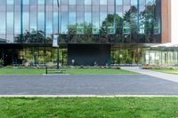 a large glass building next to a green park and grass area with benches on the walkway