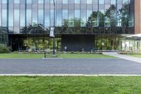 a large glass building next to a green park and grass area with benches on the walkway