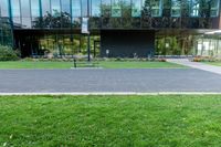 a large glass building next to a green park and grass area with benches on the walkway