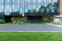 a large glass building next to a green park and grass area with benches on the walkway