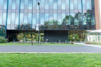 a large glass building next to a green park and grass area with benches on the walkway