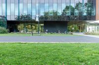 a large glass building next to a green park and grass area with benches on the walkway