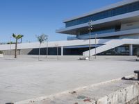 an empty parking lot in front of a building with curved glass windows and stairs on the ground