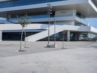 an empty parking lot in front of a building with curved glass windows and stairs on the ground