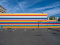 an empty parking lot painted brightly stripes on the wall of the building and sky as well as stones