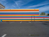 an empty parking lot painted brightly stripes on the wall of the building and sky as well as stones