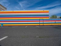 an empty parking lot painted brightly stripes on the wall of the building and sky as well as stones