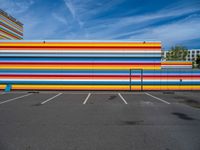 an empty parking lot painted brightly stripes on the wall of the building and sky as well as stones