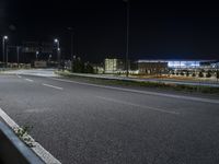 an empty highway with a street sign in front of it at night time in the background are multiple other buildings and lights