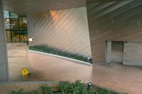 a building with a concrete wall on top with metal cladding and plants below that sits outside