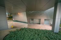 a building with a concrete wall on top with metal cladding and plants below that sits outside