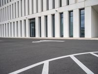 empty parking lot with white lines in the middle of it and a building behind it