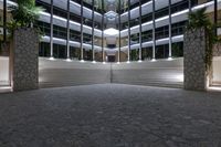 an empty lobby with many trees, lit up by daylight coming through windows, and stone steps in front