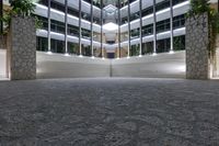 an empty lobby with many trees, lit up by daylight coming through windows, and stone steps in front