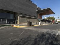 an empty parking lot with a building that has a walkway in front of it and cars parked by the curb