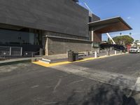 an empty parking lot with a building that has a walkway in front of it and cars parked by the curb