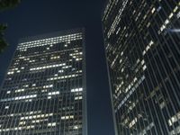 a couple of tall buildings that are lit up at night as seen from the ground