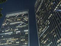 a couple of tall buildings that are lit up at night as seen from the ground