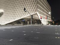 the large building has many triangular shapes in front of it at night time in front of a stop light