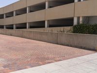 a parking garage with two entrances and a red brick sidewalk with some bushes on the side