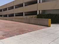 a parking garage with two entrances and a red brick sidewalk with some bushes on the side